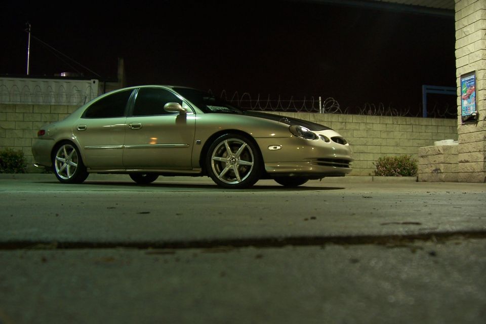 Tan sedan parked at night, showing its front quarter view, with a black hood accent