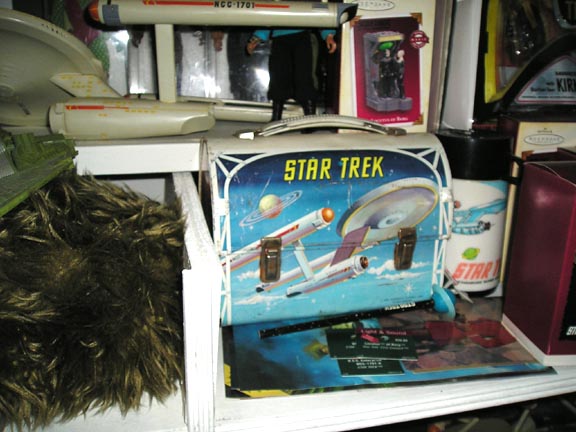 Star Trek lunchbox with Enterprise graphic, NCC-1701 model, and other collectibles on a shelf