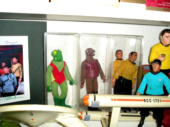 Star Trek action figures, including a green alien and crew members, displayed with a model USS Enterprise ship
