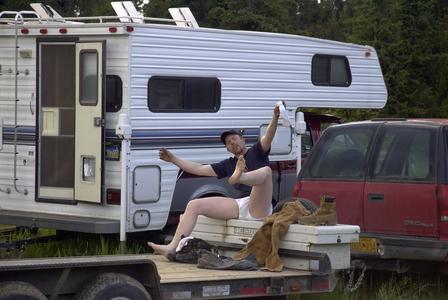 2000 Ford E350 - A man relaxes on a trailer, with a camper and a red SUV parked nearby.