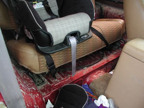 1998 Jeep TJ - The interior of a red vehicle is shown, a child car seat and a floor covered in dirt and debris.
