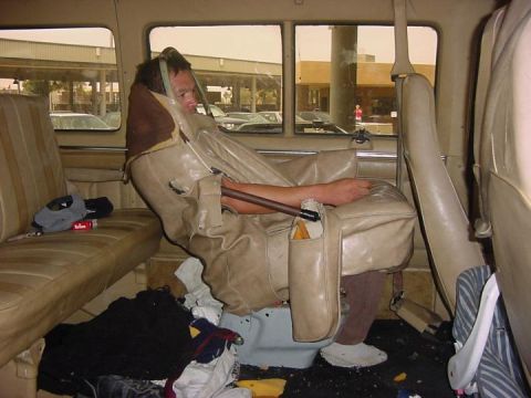 1995 Ford Bronco - A person is seated in a vehicle's interior, appearing to be in a makeshift arrangement with a tarp.