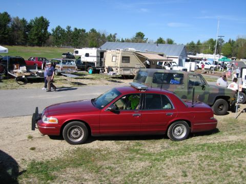1991 Ford LTD Crown Victoria - A red sedan with a light bar and push bumper is parked on grass, with other vehicles and RVs in the background.