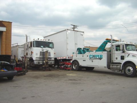 1992 Ford Bronco - A tow truck is positioned to move a semi-trailer, with a large truck in the background.