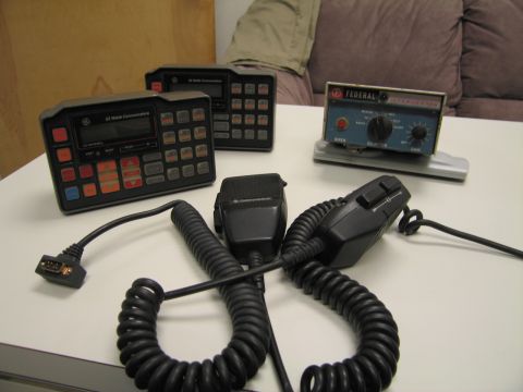 1991 Ford LTD Crown Victoria - Two GE Mobile Communications radio control heads and a Federal Signal siren control box sit on a table with two coiled-cord handheld microp…