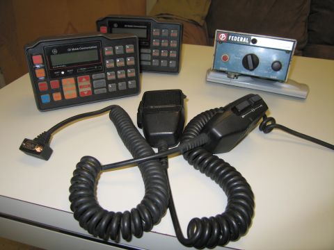 1991 Ford LTD Crown Victoria - GE Mobile Communications radio control head and a Federal siren control unit with two coiled-cord handheld microphones laid out on a table.
