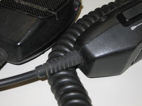 1991 Ford LTD Crown Victoria - Close-up of two black handheld microphones and their coiled cords meeting at a connection point on a white surface.