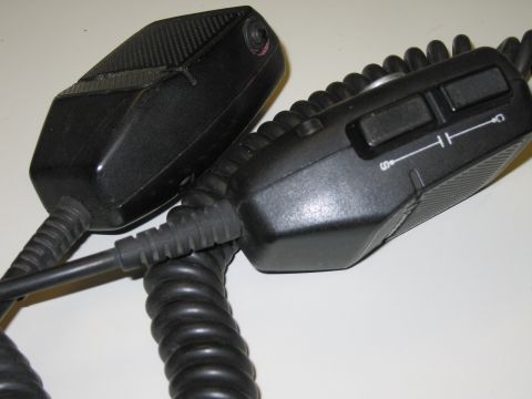 1991 Ford LTD Crown Victoria - Two black handheld microphones rest on a white surface; the right one shows a two-button push-to-talk switch panel with icons.