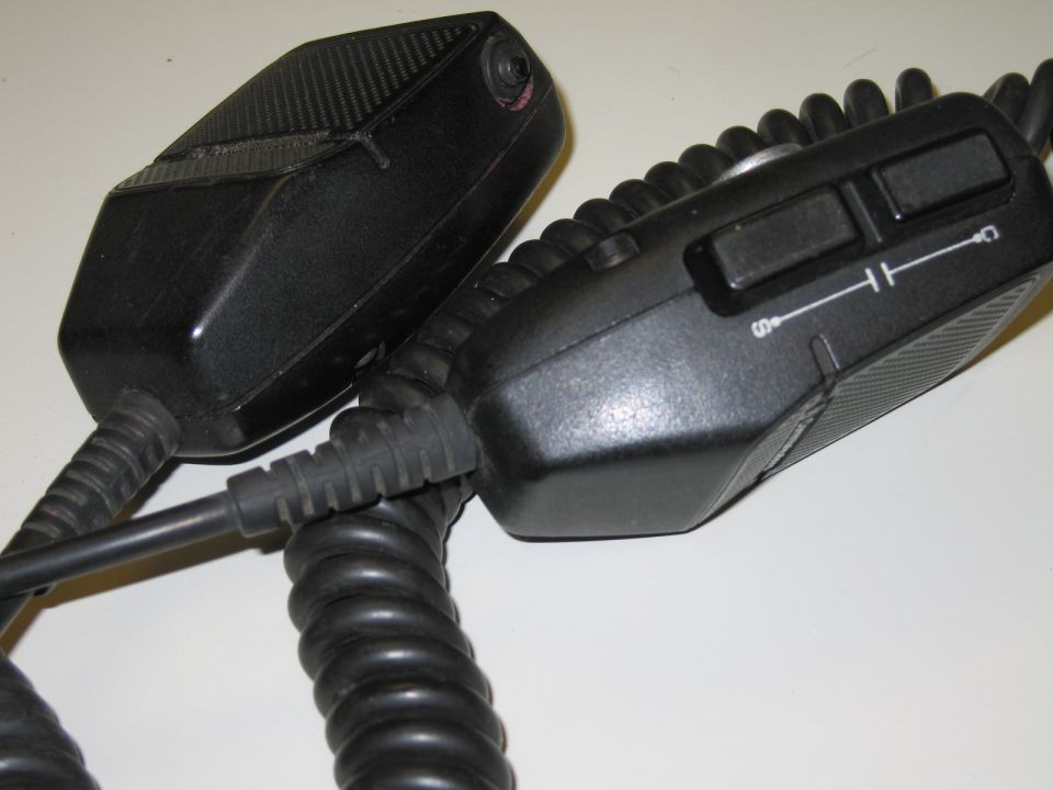 Two black handheld push-to-talk microphones, one with a two-button switch panel
