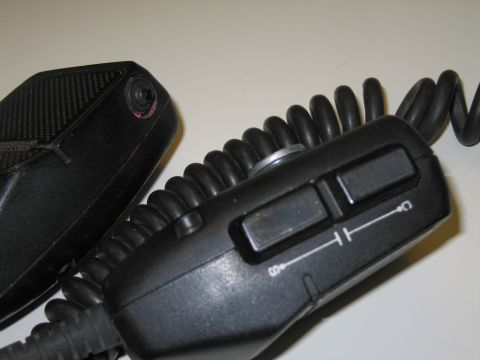 1991 Ford LTD Crown Victoria - Two black handheld push-to-talk microphones with coiled cords on a white surface, the right one marked with small switch icons.
