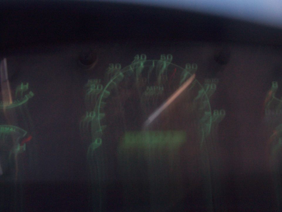 Green-lit truck speedometer at night, needle past 60 MPH, blurred by camera shake