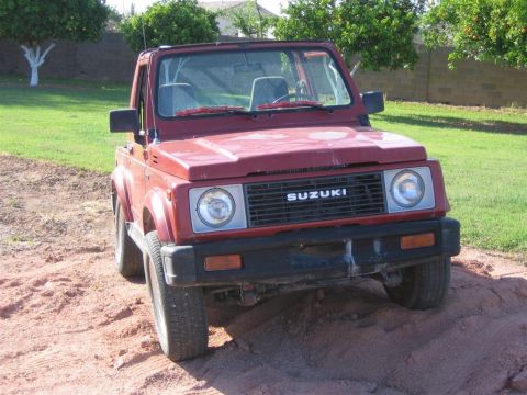 1987 Suzuki Samurai - Suzuki Samurai parked on a dirt mound, showing its front grille and headlights.