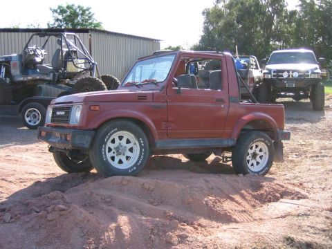 1987 Suzuki Samurai - A red Suzuki Samurai is parked on a dirt mound, with other off-road vehicles in the background.