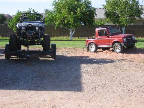 1987 Suzuki Samurai - Two off-road vehicles are parked outside on a sunny day, one on a trailer.