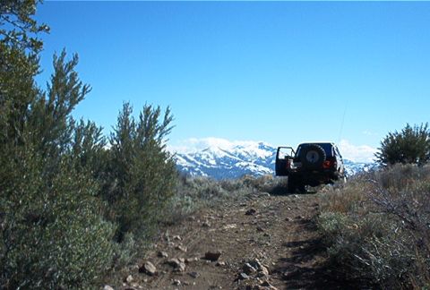 1986 Ford Bronco - Off-road vehicle parked on a dirt trail with snow-capped mountains in the background.