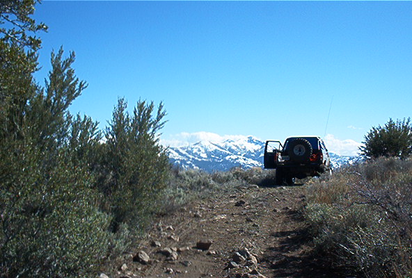 Off-road vehicle parked on a dirt trail with snow-capped mountains in the background