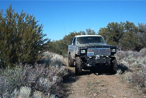 1986 Ford Bronco - This modified 1986 Ford Bronco navigates a dusty trail surrounded by arid brush under a clear blue sky.