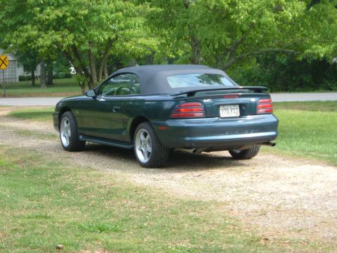 1995 Ford Mustang - This 1995 Ford Mustang convertible is parked on a gravel driveway with green trees in the background.