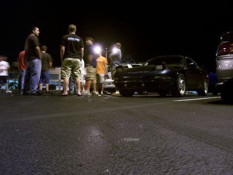 1994 Ford Probe - A group of people stand around a black coupe at night, illuminated by streetlights.