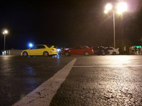 1994 Ford Probe - Several sports cars are lined up at a parking lot at night, illuminated by streetlights.