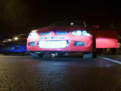 1994 Ford Probe - A red Mitsubishi Lancer Evolution is parked with its door open, alongside a blue car at night.