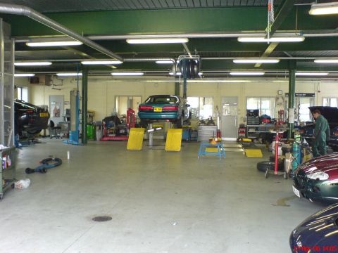 1994 Ford Thunderbird - A teal coupe is elevated on a lift inside a busy auto repair shop.