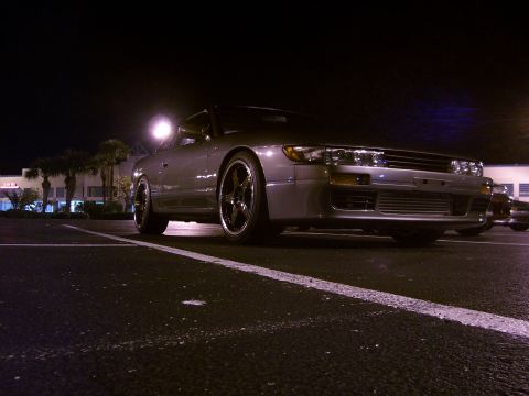 1994 Ford Probe - A silver coupe with aftermarket wheels is parked in a lot at night.