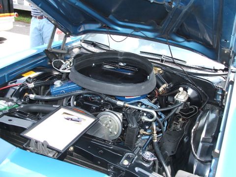 1972 Ford Ranchero - The engine compartment of a blue 1972 Ford Ranchero is displayed with the hood raised. A small informational board sits on the engine.