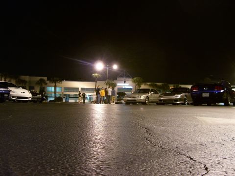 1994 Ford Probe - Several cars are parked in a lot at night, with a group of people standing near a building.