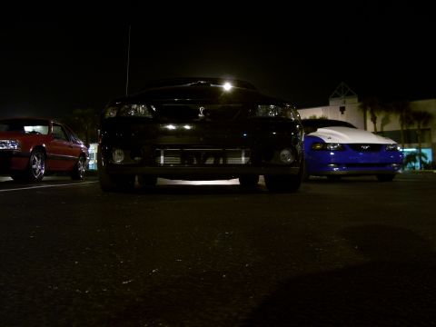 1994 Ford Probe - Three cars are parked in a lot at night, with the front of a black car in focus.