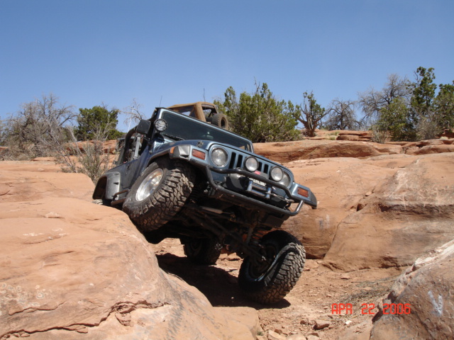 Dark Jeep Wrangler soft-top climbing slickrock ledge with mud tires on red sandstone trail