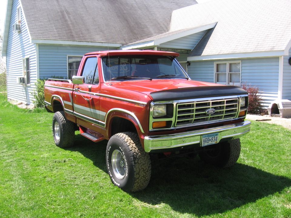Red pickup truck parked on grass in front of a house. It has a chrome grille and bumper, and a visor over the windshield