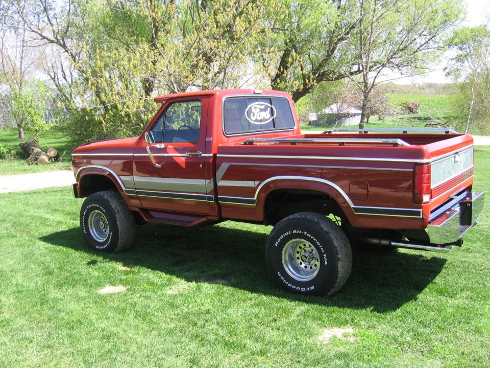 Red 1980s Ford F-150 pickup truck, side view, lifted with off-road tires