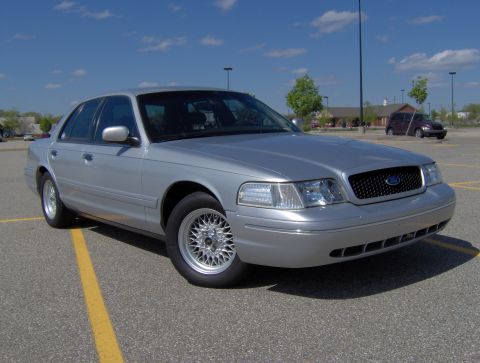 2002 Ford Crown Victoria - A silver 2002 Ford Crown Victoria is parked in a lot under a blue sky.