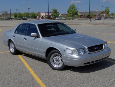 2002 Ford Crown Victoria - A silver 2002 Ford Crown Victoria is parked in a lot, showing its front grille and headlights.