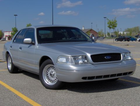 2002 Ford Crown Victoria - A silver 2002 Ford Crown Victoria is parked in a lot under a blue sky.