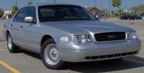 2002 Ford Crown Victoria - A silver 2002 Ford Crown Victoria is parked in a lot, showing its front grille and headlights.