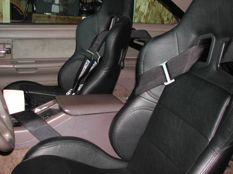 Interior shot of a car with aftermarket racing seats and harnesses. Center console and door panel visible
