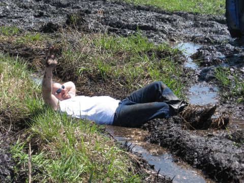 1977 Ford F-150 - A person relaxes in a muddy field, with a portion of a blue vehicle visible in the upper right corner.