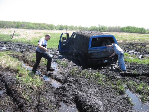 1977 Ford F-150 - Two people attempt to free a blue SUV stuck deep in mud.