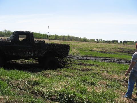 1977 Ford F-150 - A heavily mud-caked 1977 Ford F-150 is stuck in a field, with a person observing the scene.