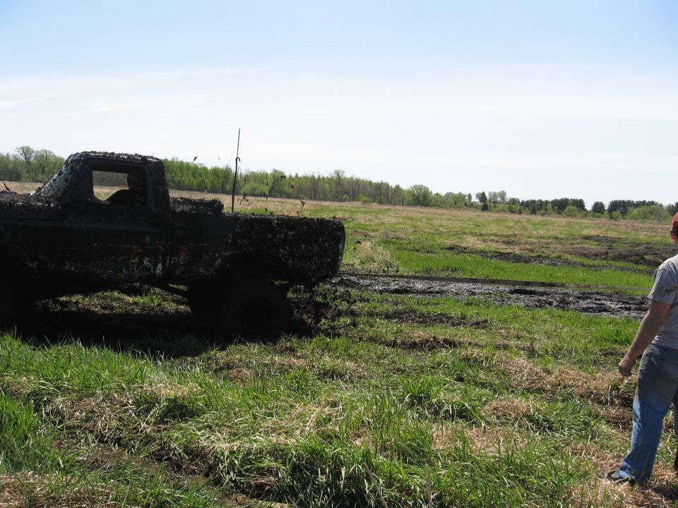 Mud-covered 1977 Ford F-150 in a grassy field with a person standing nearby