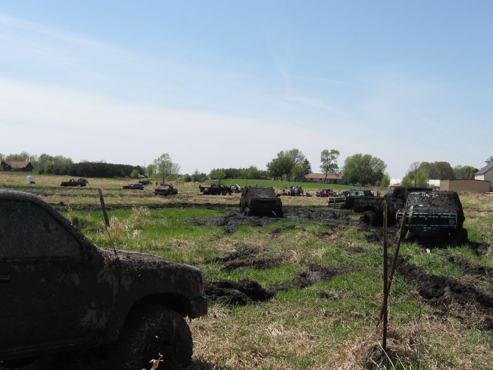 Mud-covered trucks and SUVs in a muddy field under a blue sky