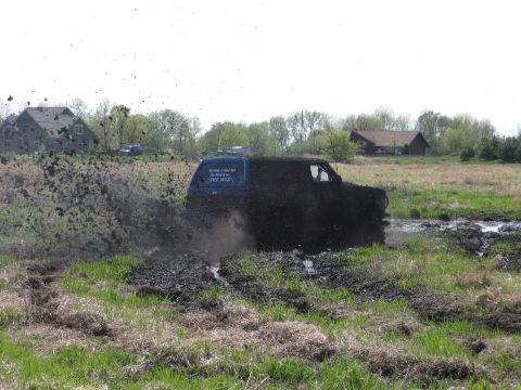 1977 Ford F-150 - A blue truck navigates a muddy obstacle course, sending mud flying.