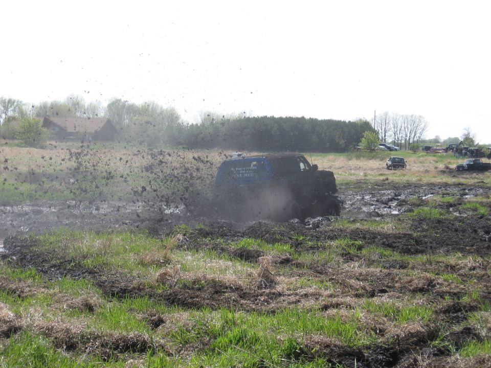 Blue SUV stuck in mud, throwing mud everywhere. Other vehicles visible in background