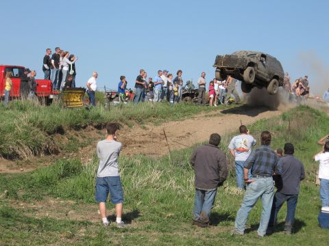 1977 Ford F-150 - A crowd watches as an SUV launches off a dirt ramp during an off-road event.