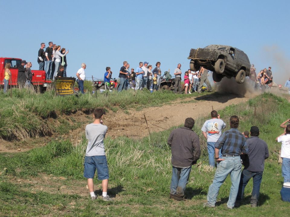 SUV airborne over dirt ramp with crowd watching