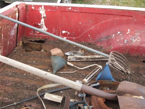 1972 Ford Ranchero - The bed of a red truck is filled with various rusty tools and debris, showing significant wear and tear.