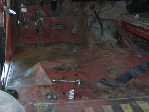 1978 Ford Bronco - The interior floor of a vehicle shows signs of rust and wear, with tools scattered around.