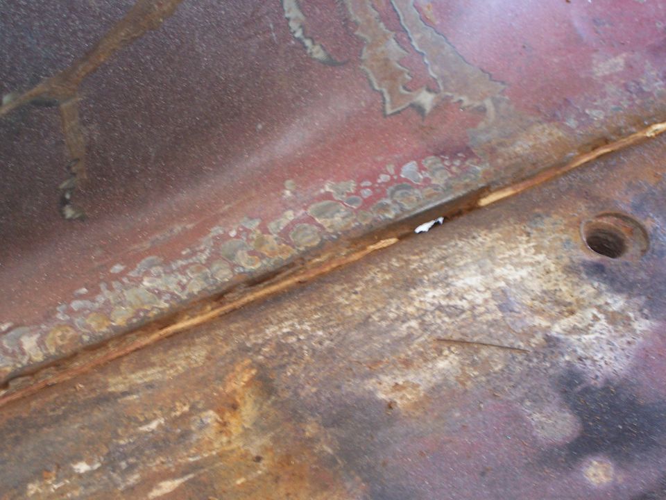 Rusted metal panel with red paint and a hole